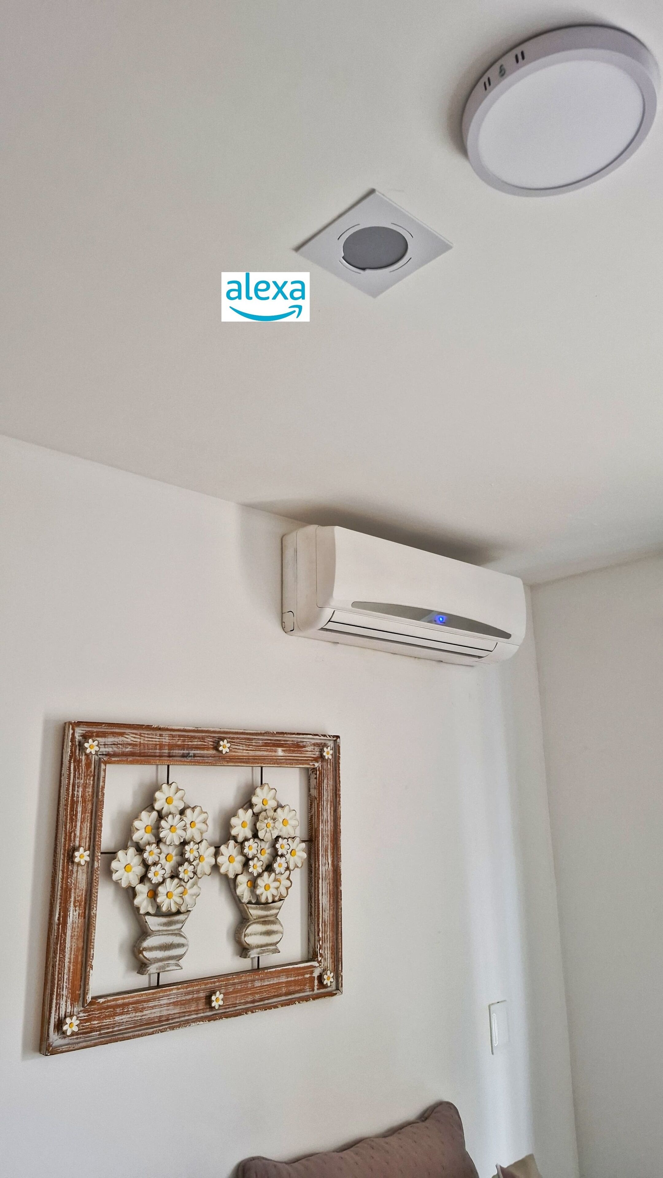 A ceiling with a circular light fixture, an air conditioning unit, and a decorative wall piece.