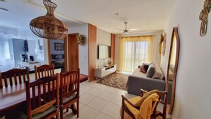 A modern living room with a sofa, a dining table with chairs, a TV, and a ceiling fan.