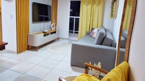 A living room with a sofa, a TV, a wooden chair, a ceiling fan, and a large mirror.