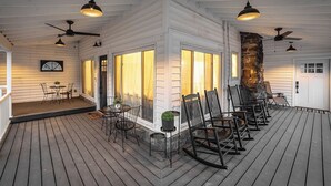 A covered porch with wooden flooring, outdoor seating, and ceiling fans.