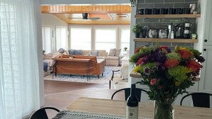 A dining area with a table set for two, a vase of flowers, and a bottle of wine.