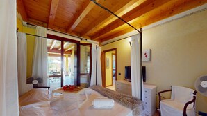 Une chambre avec un plafond en bois, un lit recouvert de draps blancs, une table de chevet, une chaise et un ventilateur.