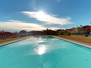 A rectangular swimming pool with clear blue water, surrounded by well-maintained lawns and a few buildings in the background. - Garda Pleasure By Bookinggardalake (Padenghe sul Garda)