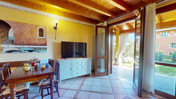 Un espace repas comprenant une table en bois, des chaises, un téléviseur et une vue sur l’extérieur.