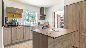 A modern kitchen with wooden cabinets, a central island, and a built-in stove. - CHARMING VILLA WITH HEATED POOL OVERLOOKING THE GOLF COURSE (SEIGNOSSE)
