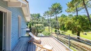 A wooden deck with two lounge chairs, a metal railing, and a view of a golf course and trees. - CHARMING VILLA WITH HEATED POOL OVERLOOKING THE GOLF COURSE (SEIGNOSSE)