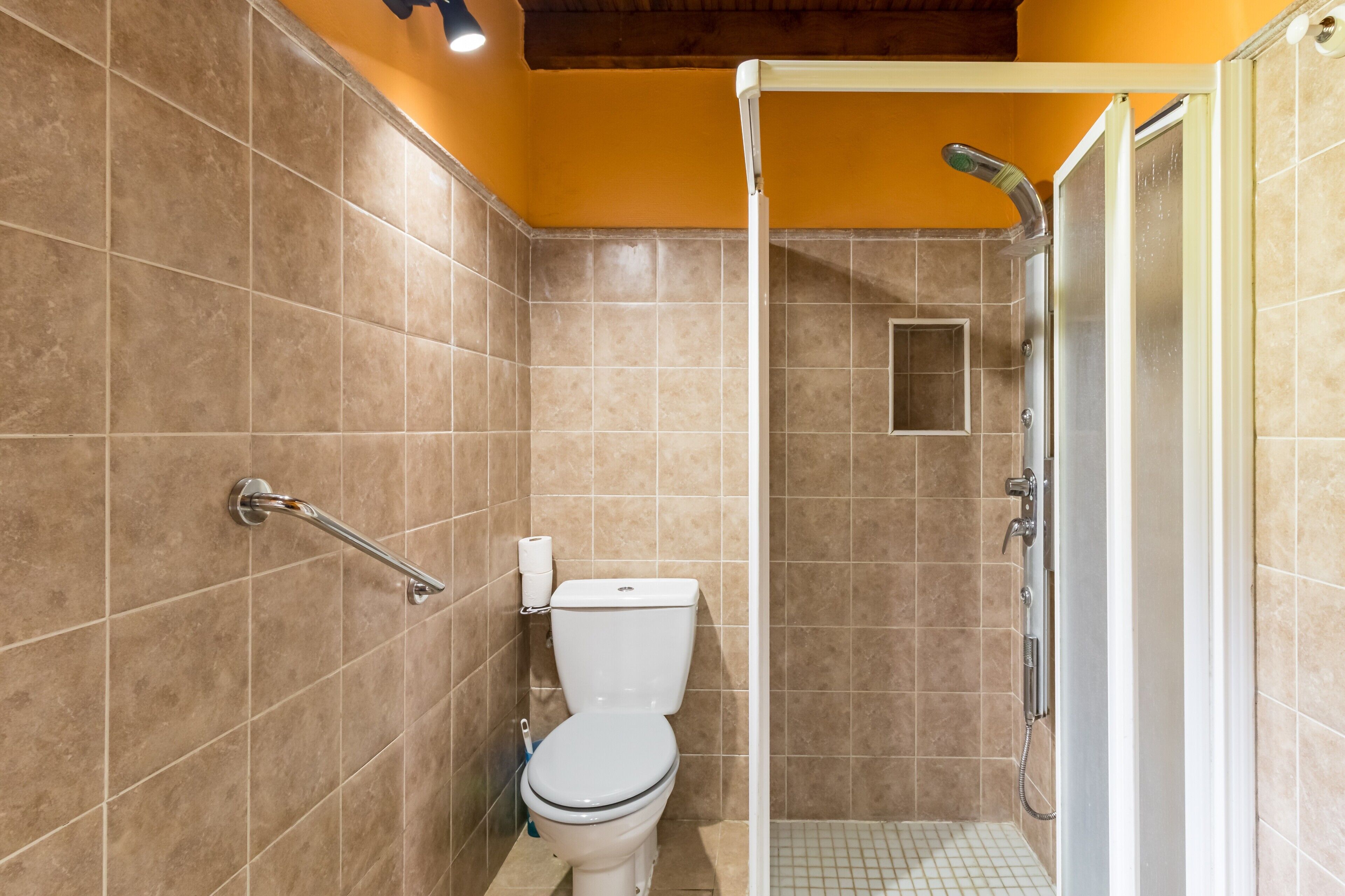 Un baño con ducha, inodoro y barra de apoyo.
