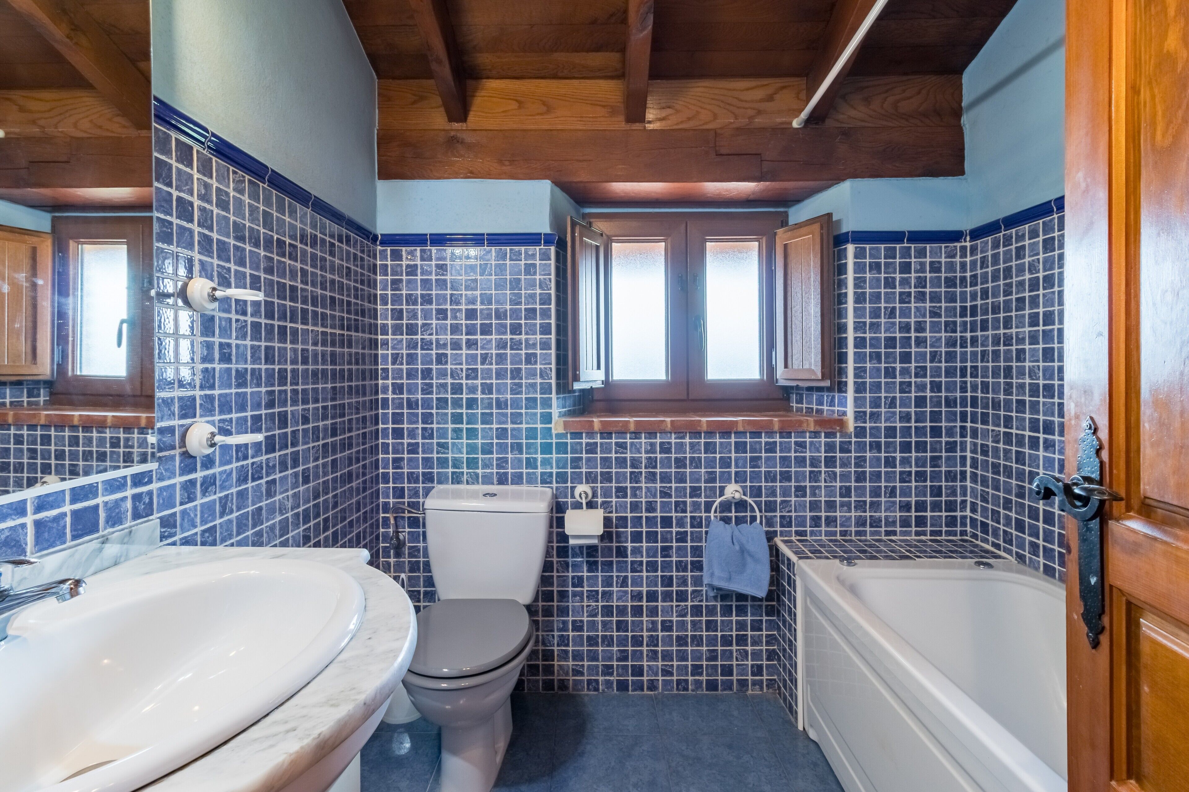 Un baño con inodoro, lavamanos, bañera y paredes con azulejos azules.