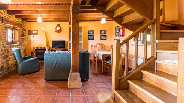 Een rustiek interieur met een stenen muur, een houten trap en een gezellige zithoek met een open haard.