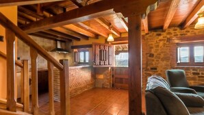 Een rustiek interieur met zichtbare houten balken, een stenen muur, een keukenhoek en een zithoek met uitzicht.
