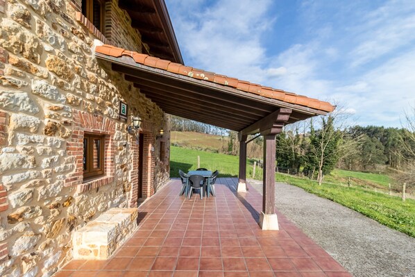 Un edificio de piedra con un porche cubierto, mobiliario al aire libre y vistas a un paisaje verde.