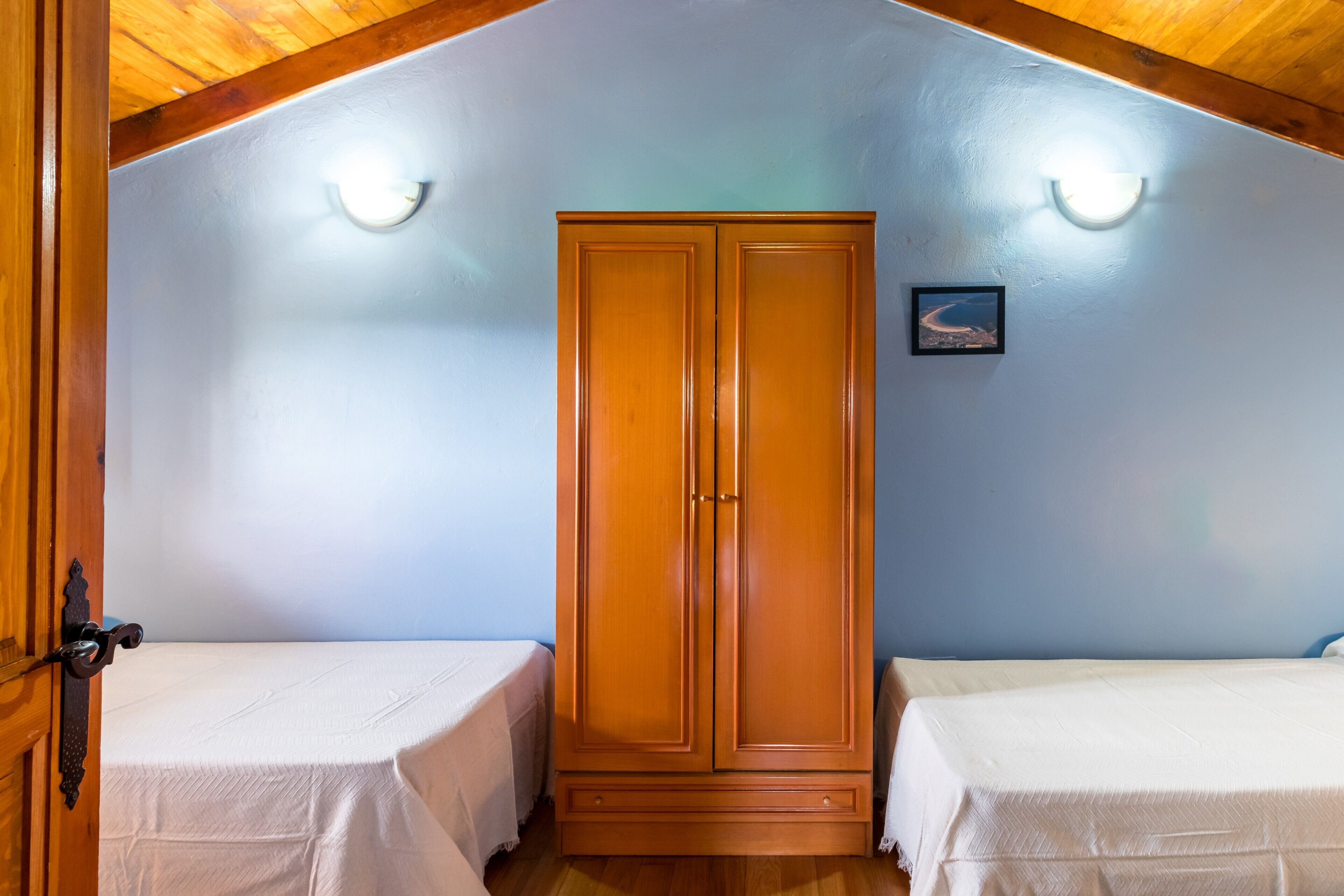 Een kamer met twee eenpersoonsbedden, een houten garderobe en een schuin plafond.