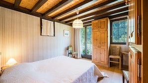 A bedroom with a large bed, wooden ceiling beams, a window with a view of trees, and a wooden cabinet. - Chalet 'Le Tougne' with Mountain View, Private Terrace and Balcony (Champagny-en-Vanoise)