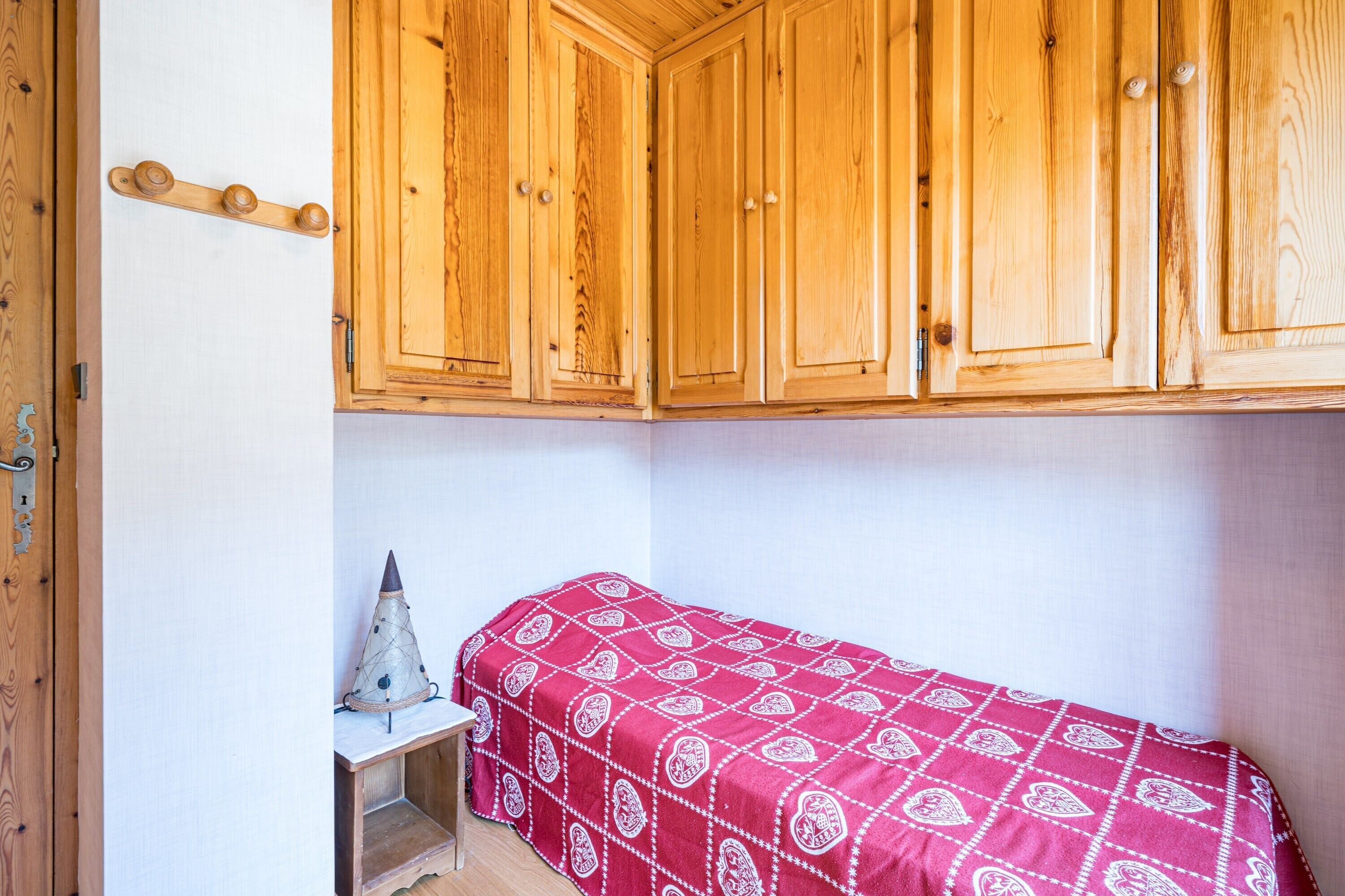 Un dormitorio pequeño con armarios de madera, una cama con cubrecama estampado y una mesita con un objeto decorativo.