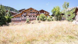 A wooden chalet with balconies, surrounded by dry grass and trees. - Chalet 'Le Tougne' with Mountain View, Private Terrace and Balcony (Champagny-en-Vanoise)