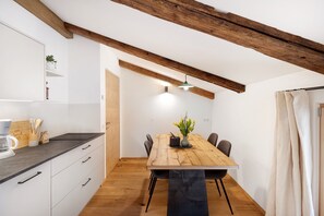 A modern kitchen with white cabinets, a wooden dining table, and a hanging light fixture.
