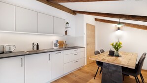 A modern kitchen with white cabinets, a wooden dining table, and a pendant light.