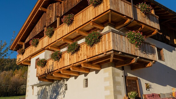 A wooden building with balconies, a stone wall, and outdoor seating.