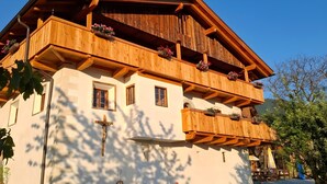 Een houten chalet met meerdere verdiepingen, balkons, een kruis en buitenmeubels.