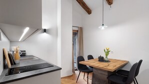 Een moderne keuken met een inductiekookplaat, een eethoek met een houten tafel en zwarte stoelen, en een zichtbaar raam.