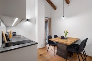 A modern kitchen with an induction cooktop, a dining area with a wooden table and black chairs, and a visible window. - Apartment 'Lauterfresser' with Mountain View, Shared Garden and Wi-Fi (Rodeneck)