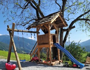 A wooden play structure with a slide, swings, and a small car. - Apartment 'Lauterfresser' with Mountain View, Shared Garden and Wi-Fi (Rodeneck)