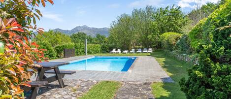 A swimming pool with lounge chairs, a stone pathway, and lush greenery.