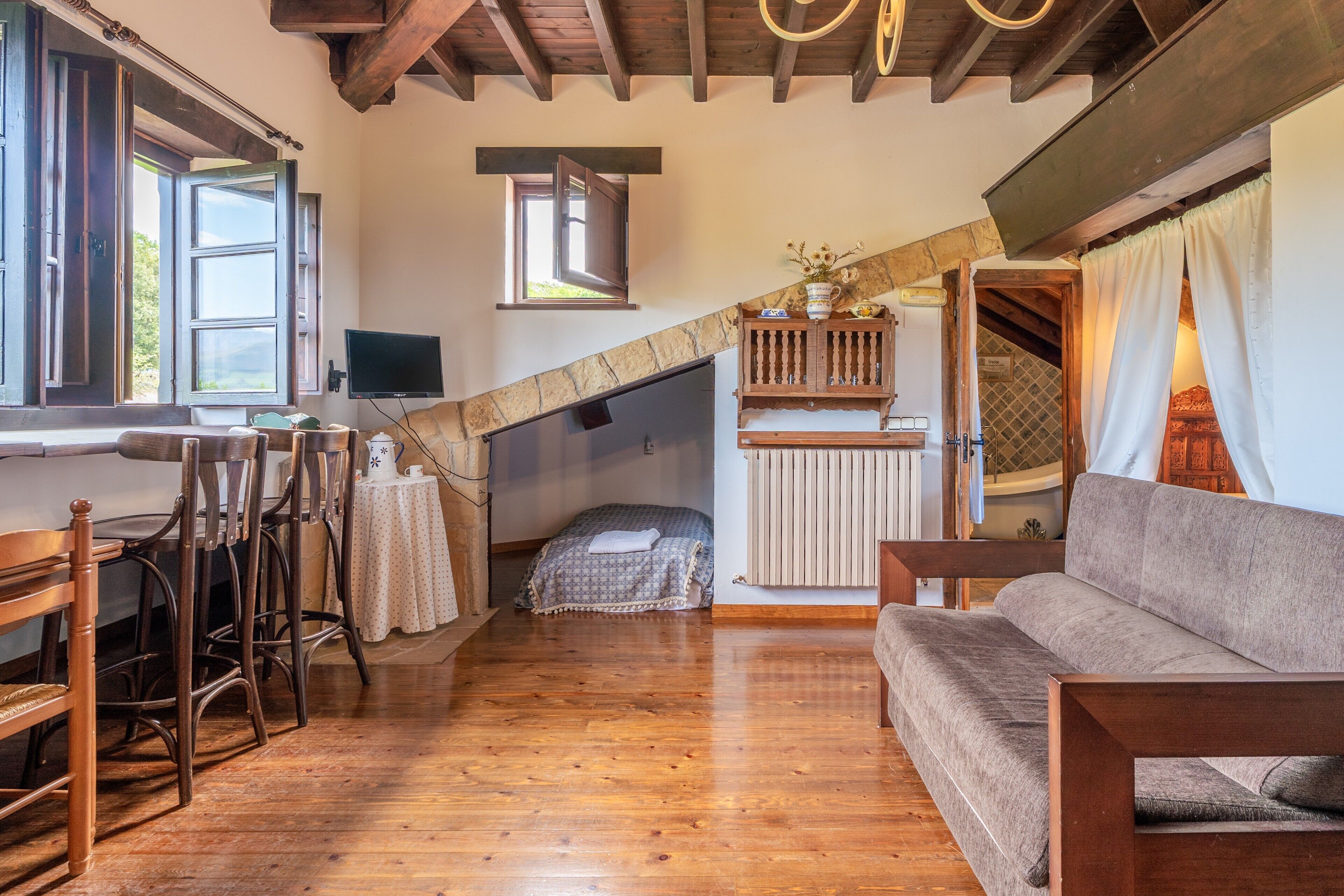 A room with wooden floors, a sofa, a dining table with chairs, a TV, and a window with curtains.