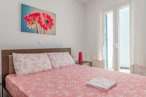 Un dormitorio con una cama, almohadas, una mesita de noche, una lámpara y un cuadro de flores.