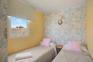 A bedroom with two beds, a window, and a floral wallpaper.