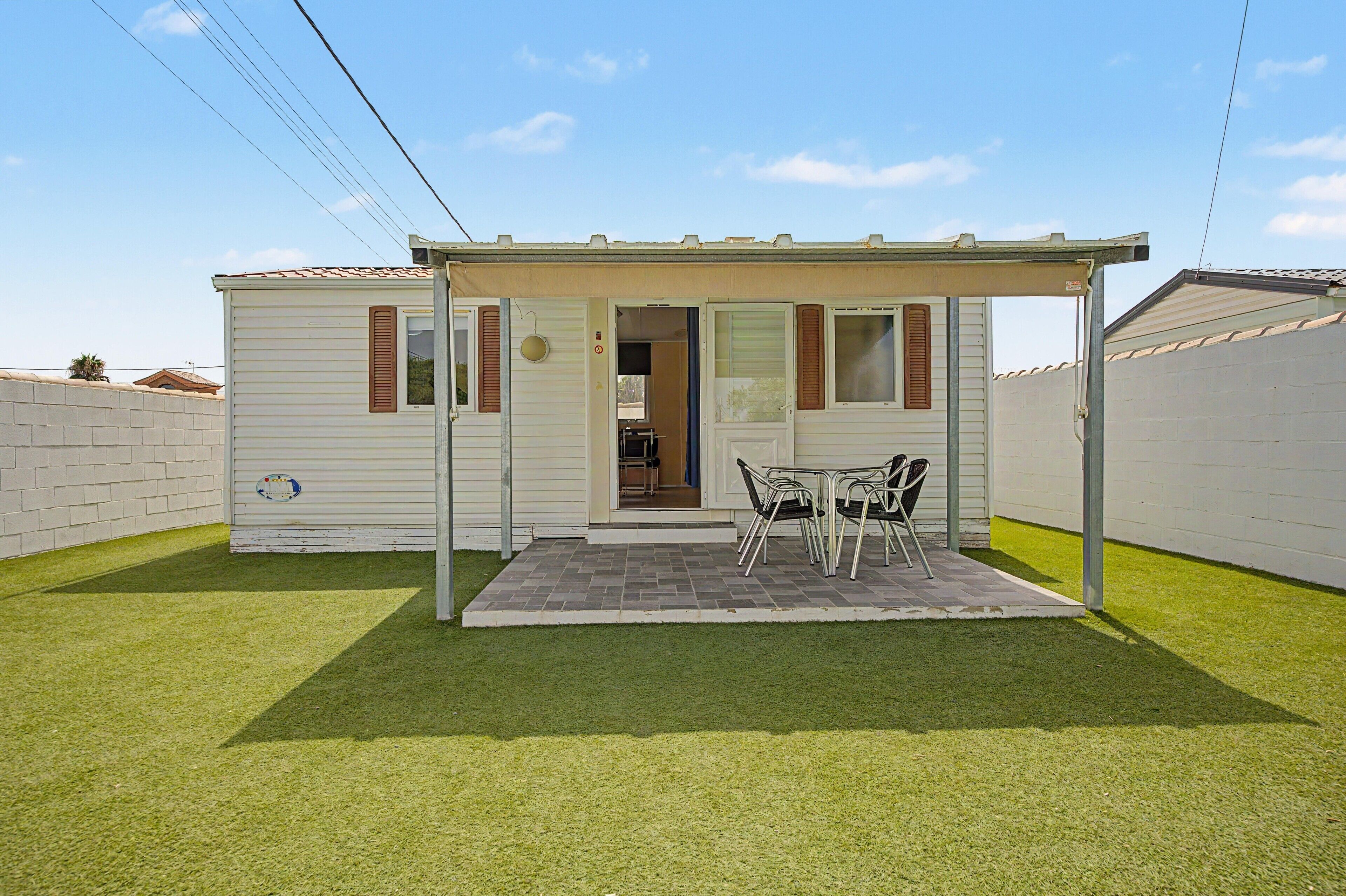 A small, single-story building with a covered patio area, a table and chairs, and a door leading to an interior space.