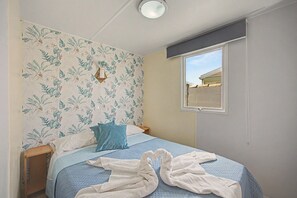 Un dormitorio con cama, ventana y pared decorada con motivos de hojas tropicales.