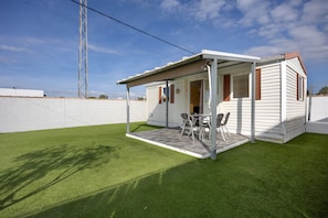A mobile home with a patio area, a table with chairs, and a white fence in the background.