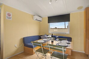 Una habitación compacta con una mesa de comedor para dos personas, un banco acolchado azul, una ventana con vistas y una unidad de aire acondicionado instalada en el techo.