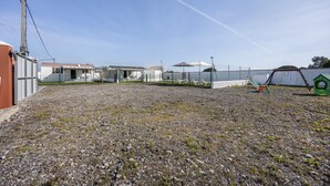 A gravel yard with a playground, a building with a red roof, and a fence. - Holiday Home 'El Olivo 2' with Shared Pool, Wi-Fi & Air Conditioning (Chiclana de la Frontera)