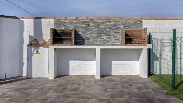 A barbecue area with a stone backsplash, a fenced enclosure, and a warning sign. - Holiday Home 'El Olivo 2' with Shared Pool, Wi-Fi & Air Conditioning (Chiclana de la Frontera)