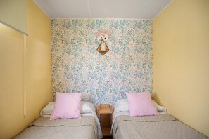 Una habitación con dos camas, un papel tapiz floral y un adorno colgante.