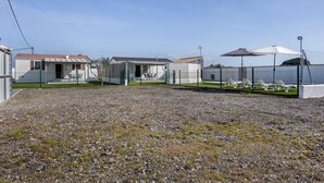 A row of mobile homes with a gravel driveway, a fenced area with lounge chairs, and a clear sky. - Holiday Home 'El Olivo 2' with Shared Pool, Wi-Fi & Air Conditioning (Chiclana de la Frontera)