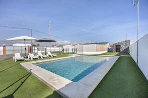 Une piscine bordée de gazon synthétique, avec des chaises longues et des parasols.