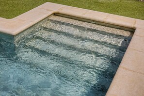 Une piscine bordée de pierres, entourée d’une pelouse.