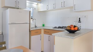 Una cocina moderna con armarios blancos, un refrigerador empotrado, una estufa a gas y un frutero sobre la encimera.