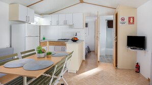 Una cocina moderna con armarios blancos, un comedor con mesa y sillas, un televisor en un estante y un extintor de incendios en la pared.