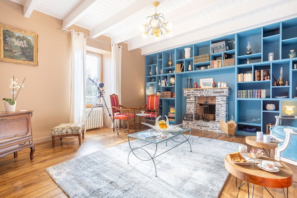 Una habitación con chimenea, una estantería azul, una mesa de centro de madera y un sillón rojo.