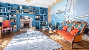 Una sala de estar con chimenea, estanterías azules, un sofá y un cuadro grande de un velero.
