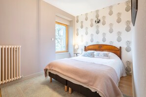 Une chambre à coucher avec un lit, une fenêtre, un radiateur et un papier peint à motifs d’ananas.