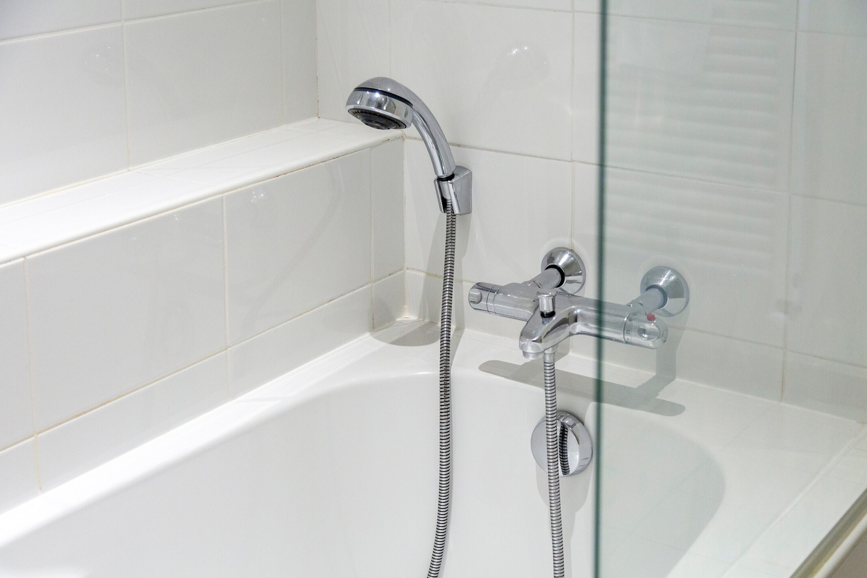 Une salle de bain moderne avec une douche à parois de verre, des robinetteries chromées et des murs recouverts de carreaux blancs.