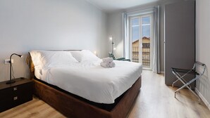 Un dormitorio con cama, mesita de noche, lámpara y vistas al exterior.