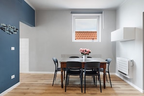 A dining area with a table, chairs, a vase of flowers, a window, and a radiator.