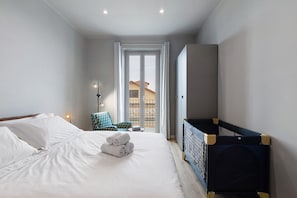 Camera da letto con un letto, una culla, una sedia e vista sul balcone.