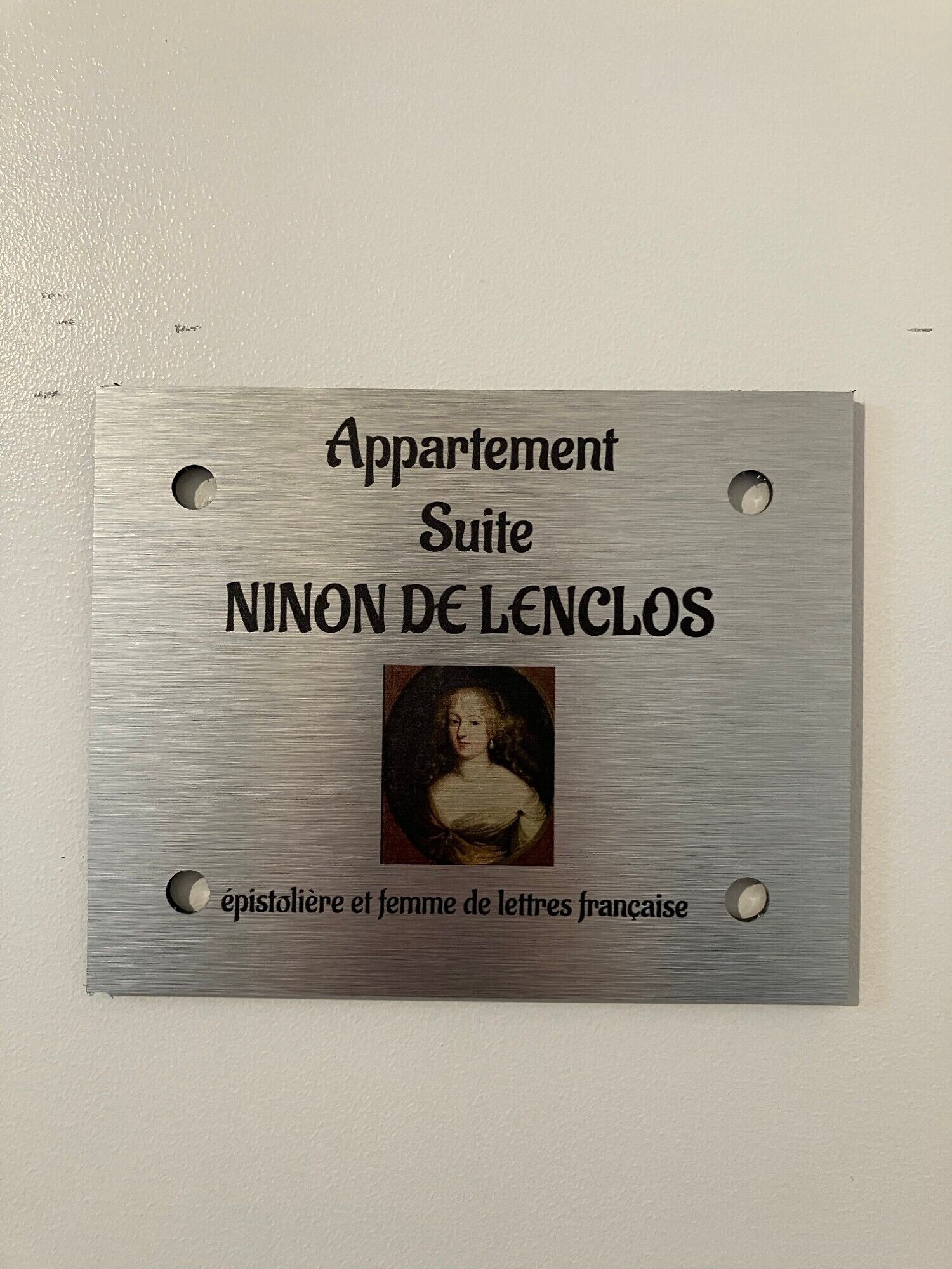 A plaque with the text 'Appartement Suite NINON DE LENCLOS' and a portrait.